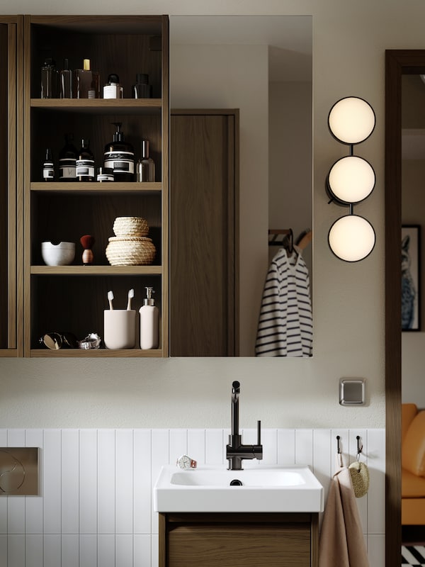 A bathroom wall with a HAGAÅN wall open cabinet with a brown oak effect and a LETTAN mirror cabinet with door.