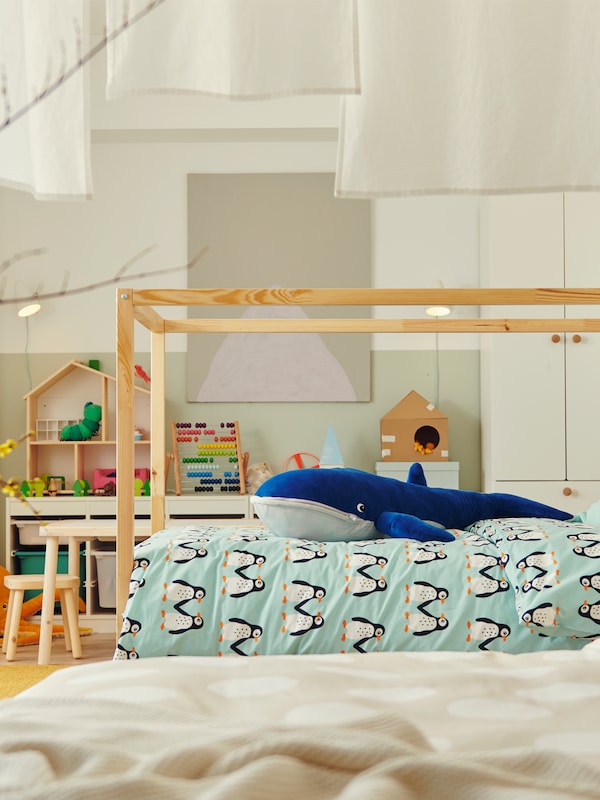 A bedroom with a KURA reversible bed covered with BLÅVINGAD bed linen and with a BLÅVINGAD blue whale soft toy on top.