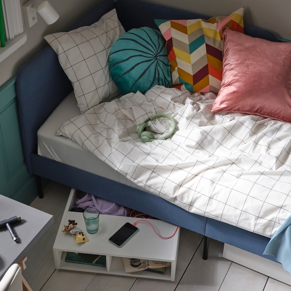 A blue upholstered bed with white/black checked VITKLÖVER bed linen and various cushions, with FREDVANG under-bed storage.