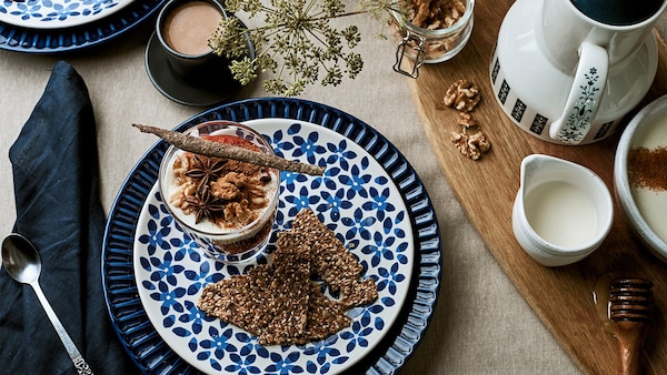 A close up of a table aid with blue decorative plates, a dessert and a pot of milk.