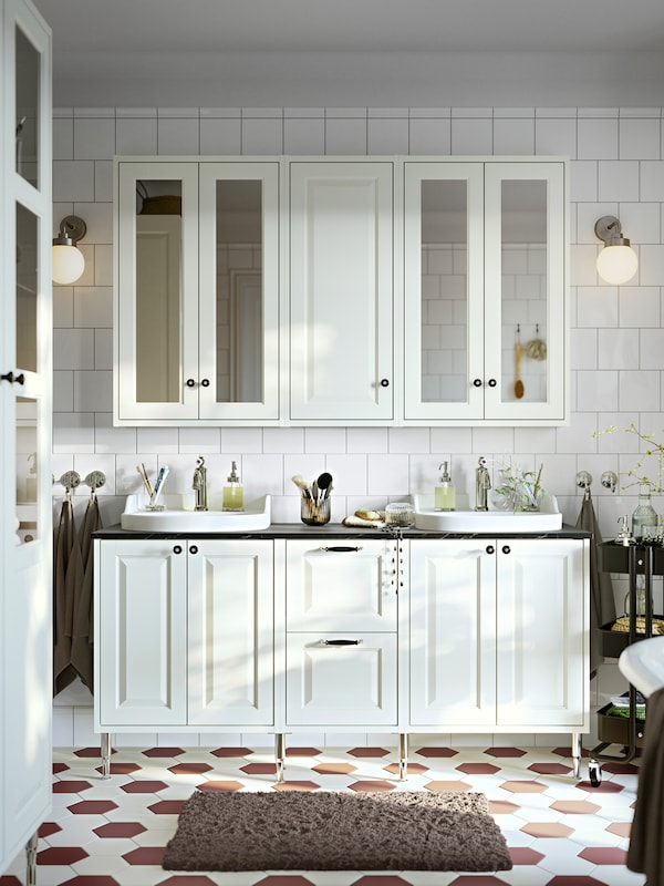 A frontal view of a bathroom with white TÄNNFORSEN wash-stands with doors and drawers and mirror cabinets with doors.