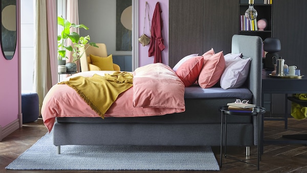 A grey and purple bedroom with grey, upholstered bed and pale pink bedding.