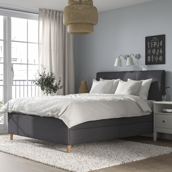 A grey bedroom with a dark grey IDANÄS upholstered bed covered with white bed linen. 
