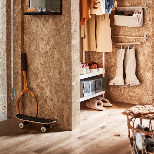 A hallway with a white coat rack with shoe storage, a rattan basket with shoes plus a rail with boots on a skirt hanger.