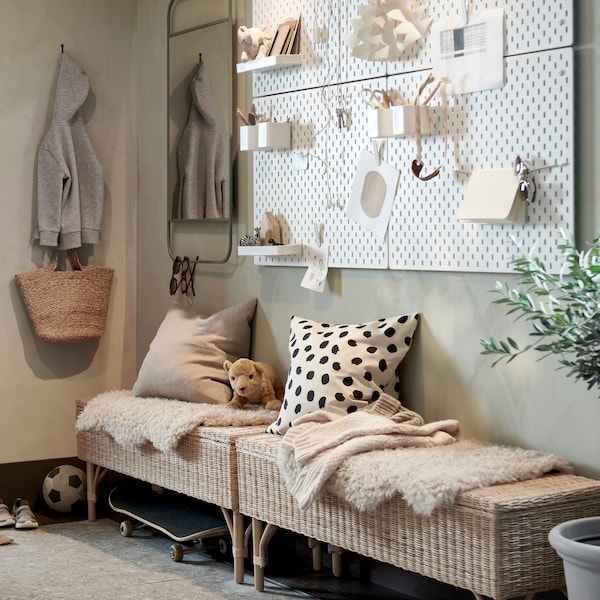 A hallway with two rattan benches with storage, a wall with white pegboards and a green mirror, plus a large potted plant.