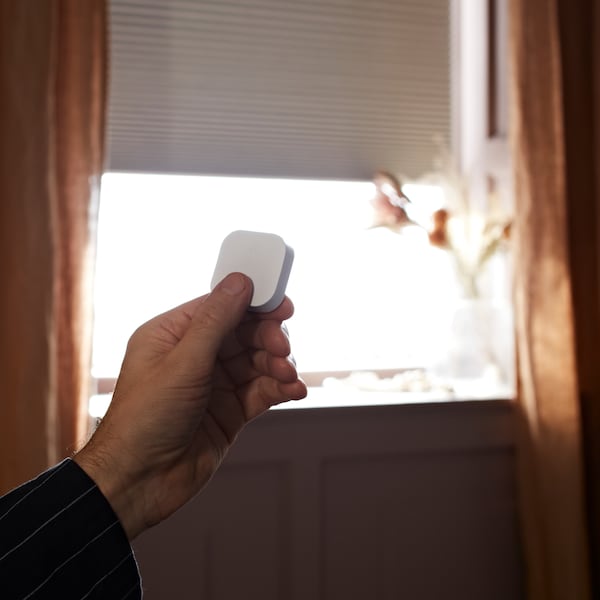 A hand uses a remote control to raise a smart wireless/battery-operated TREDANSEN block-out cellular blind.