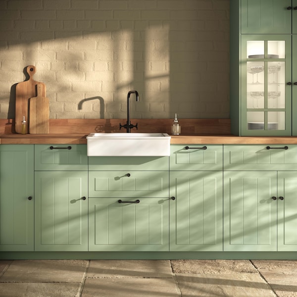 A kitchen with traditional green fronts, wood worktop and black handles.