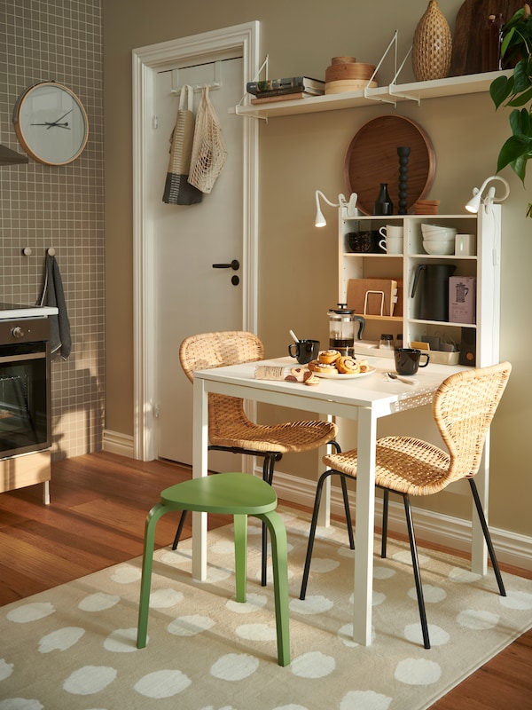 A light kitchen with ÄLVSTA rattan-seat-and-black-frame chairs around a white MELLTORP table, all placed on a BOGENSE rug.