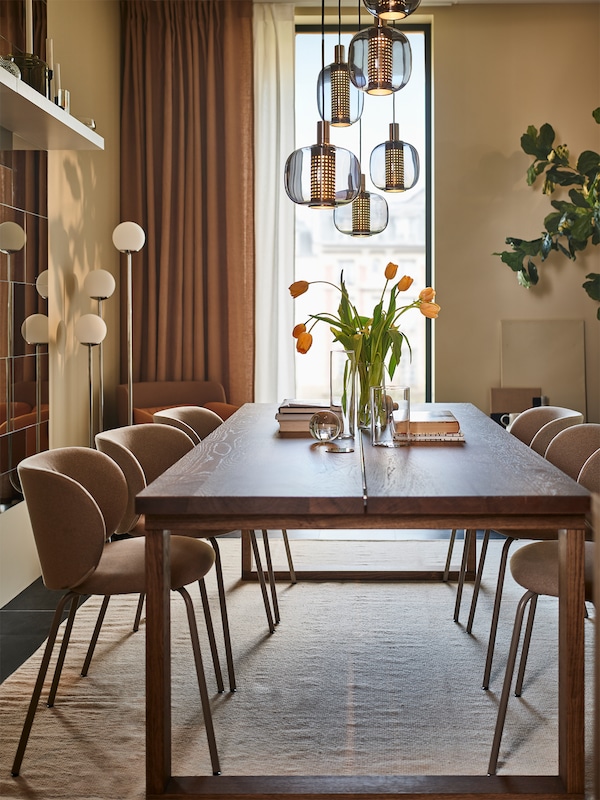 A MÖRBYLÅNGA table with a vase of tulips on top is in a narrow yet elegant dining room with six dark beige KRYLBO chairs.