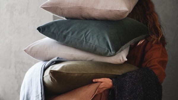 A person holding a pile of cushions with SANELA cushion cover 50x50 cm grey-green. 