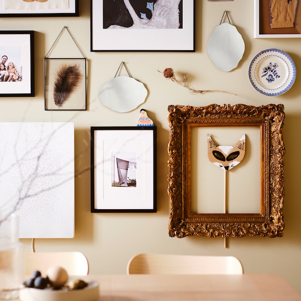 A picture wall over a birch RÖNNINGE table, with black RIBBA and LOMVIKEN frames plus other frames and decorative items.