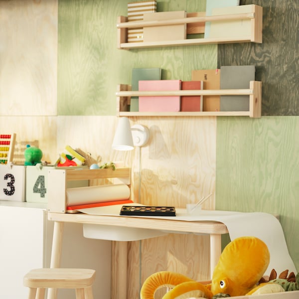 A pine FLISAT children’s table with a TROFAST storage box in its top stands under some FLISAT wall storage on the wall.