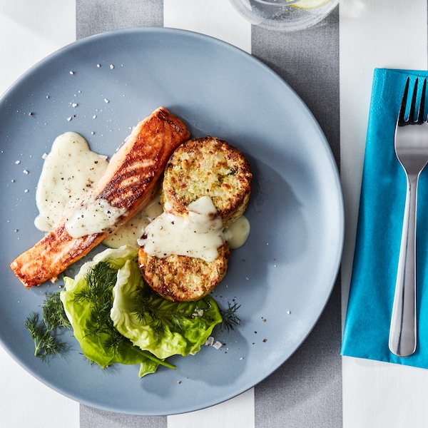 A plate of SJÖRAPPORT salmon fillet with salad, sauce, GRÖNSAKSKAKA vegetable medallions and DRAGON cutlery.