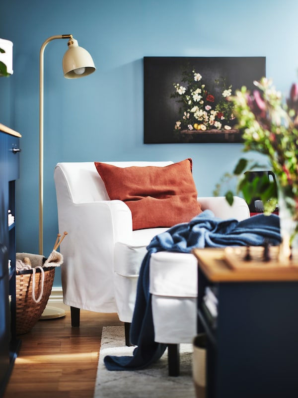 A ROCKSJÖN armchair with an extra cushion with a red-brown DYTÅG cushion cover stands in a living room with blue walls.