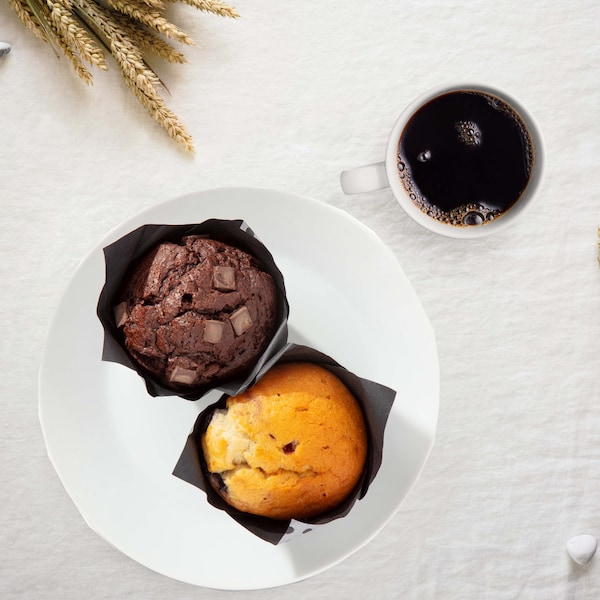 A serving plate with 2 muffins and a cup of coffee next to it