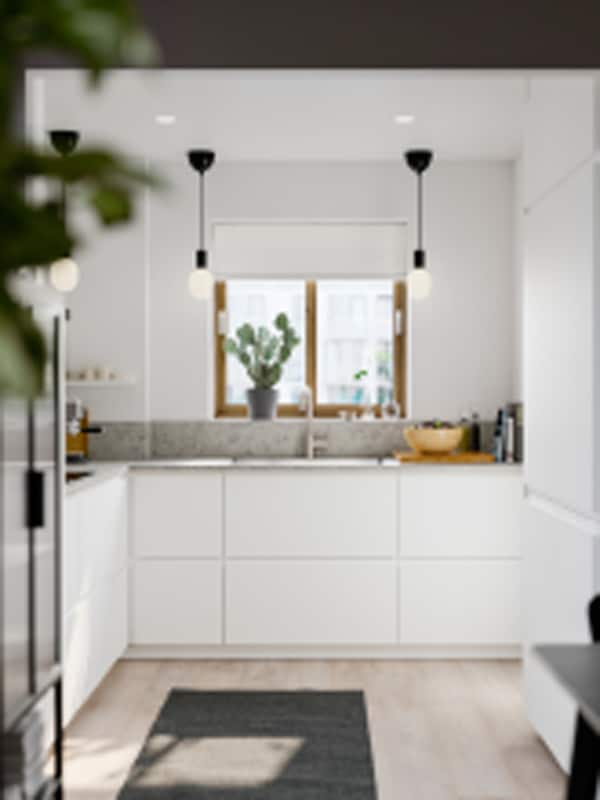 A small bright kitchen with matte white VOXTORP fronts, white walls, a grey rug on the floor and small black pendant lamps.