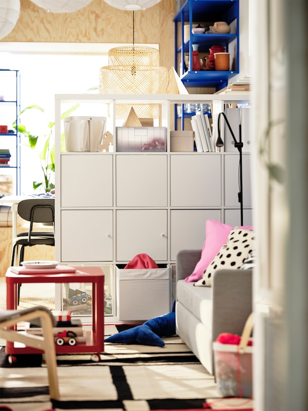 A small, colourful living room with a playful Scandi style has a white KALLAX shelving unit used as a room divider.