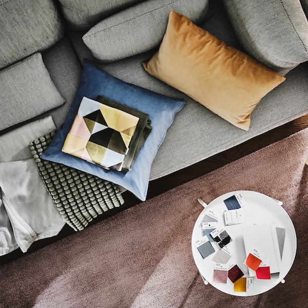 A SÖDERHAMN 3-seat sofa with cushions and a light pink throw on it is by a side table with colour swatches on it.