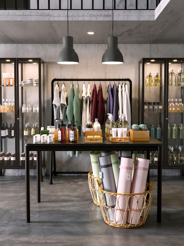 A TOMMARYD table with boxes and bottles on top of it stands in a shop underneath two HEKTAR pendant lamps.