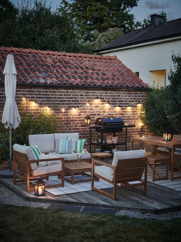 A twilight outdoor space with a NÄMMARÖ four-seat conversation set, a GRILLSKÄR barbecue and a SVARTRÅ LED lighting chain.