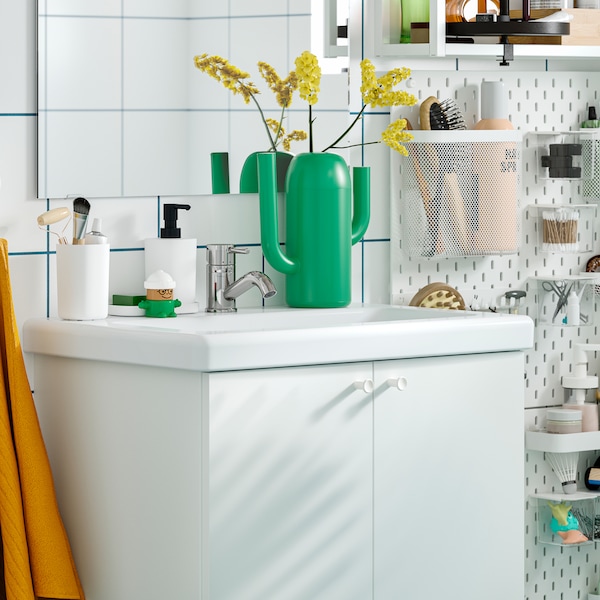 A white ENHET wash-basin cabinet with two doors and a SKÅDIS pegboard with bathroom accessories behind it.