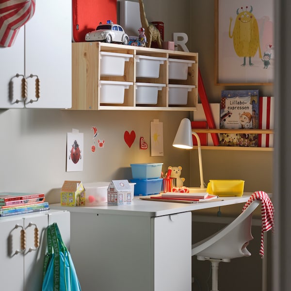 A white LÄRANDE desk with pull-out storage unit stands against a wall under some TROFAST wall storage in a child’s room.