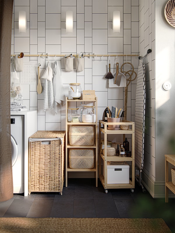 A white-tiled corner has a white washing machine, a RÅGRUND trolley, a rail on the wall and a storage shelf made of bamboo.