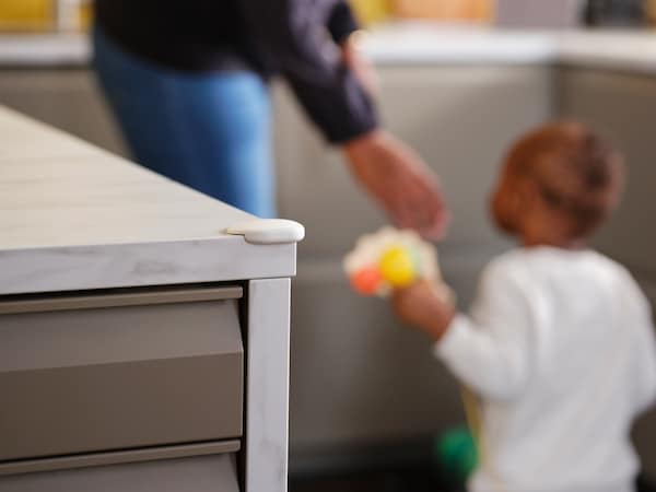 A woman and a toddler in a kitchen with a white UNDVIKA corner bumper on the corner of a white marble effect worktop.