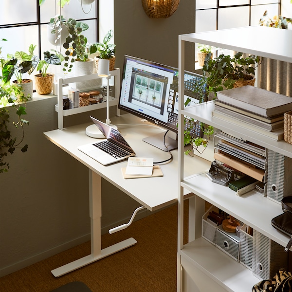 A workspace centred around a TROTTEN sit-stand desk, nestled between a white TROTTEN cabinet with sliding doors and a window.