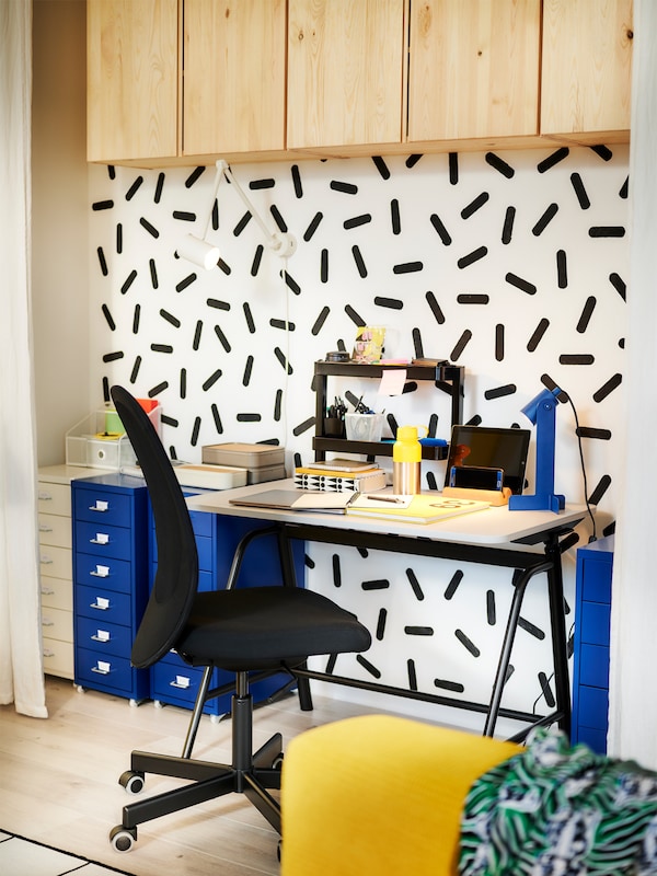 A workspace in a bright, colourful room with a GLADHÖJDEN sit-stand desk placed by a graphic-patterned wall.