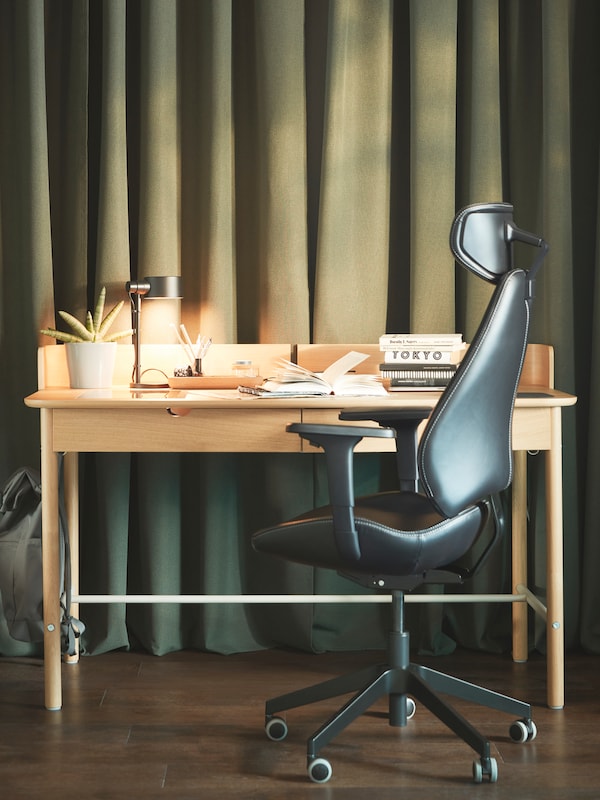 A workspace with a GRUPPSPEL gaming chair and a RIDSPÖ oak-veneer desk beneath wall-covering dark-green ROSENMANDEL curtains.