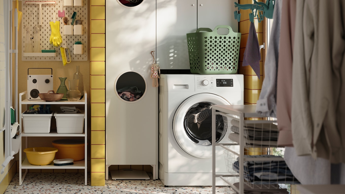 A yellow-tiled laundry room with a white NYSJÖN cabinet, a washing machine and various accessories in different colours.