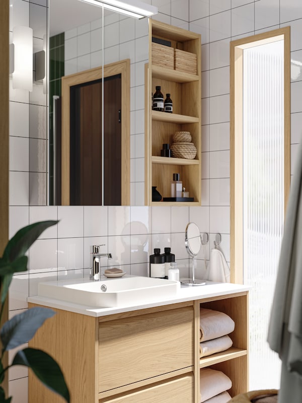 An ÄNGSJÖN washstand with drawers in oak effect is in a white bathroom with a LETTAN mirror cabinet with doors above it.