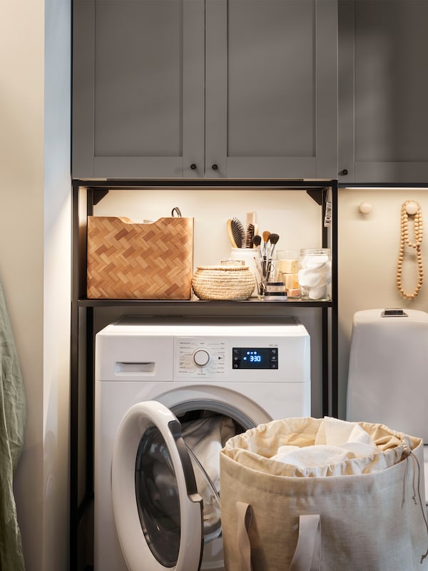 An ENHET storage combination with grey fronts is standing in a small bathroom that has an UDDARP washer/dryer combination.