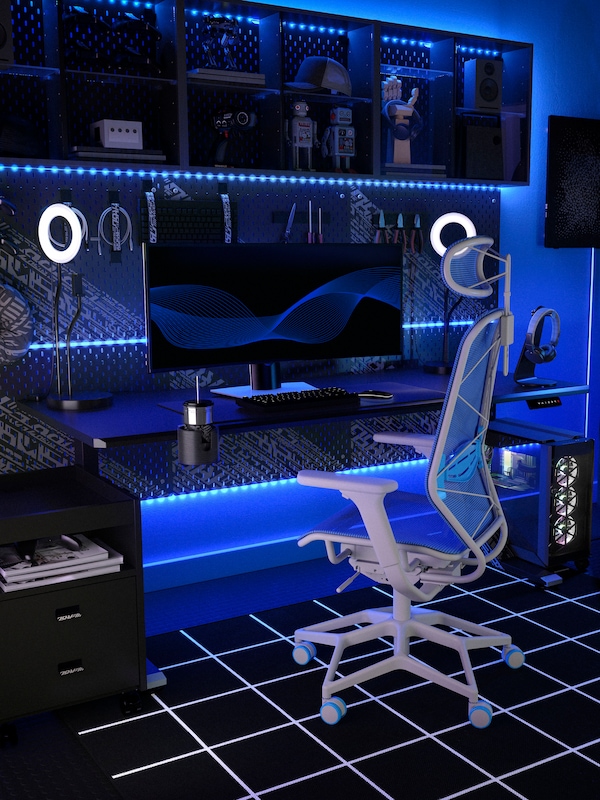 An IKEA STYRSPEL gaming chair in grey and blue in front of a black gaming desk, in a room lit with blue neon lights.