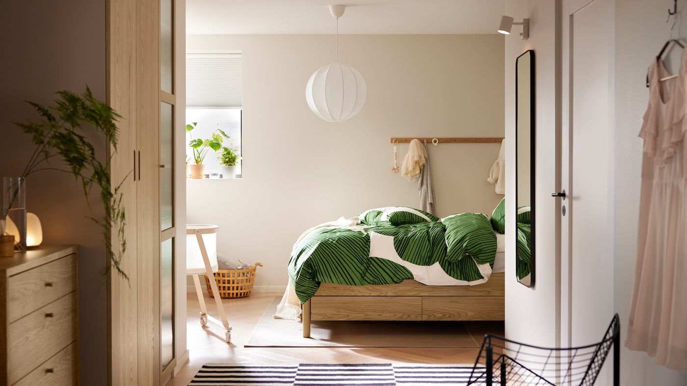 An oak veneer TONSTAD bed with storage with KUNGSCISSUS bed linen stands in a bedroom with racks with knobs on one wall.