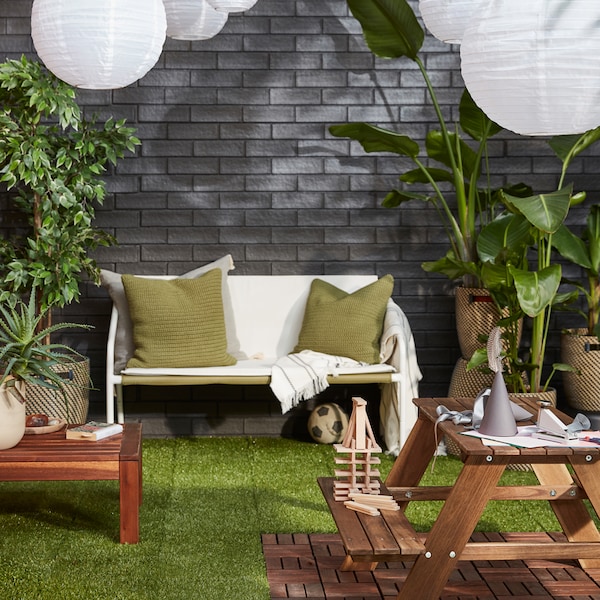 An outdoor area with a cosy seating area, lush plants, LED solar-powered pendant lamps against a grey brick wall.