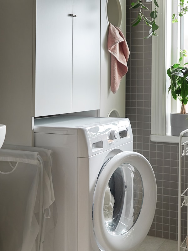 An UDDARP washing machine, a HORNAVAN trolley and a NYSJÖN cabinet, all in white, are standing next to window.
