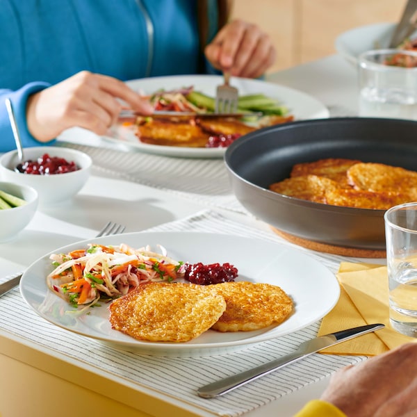 GÅNGLÅT shredded potato pancakes in a plate on the dining table, with a pan with some inside as well close by.