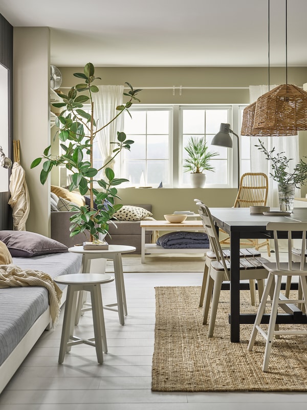 In a traditional Scandinavian dining room are a large NORDVIKEN dning table with four chairs, green plants and grey sofas.