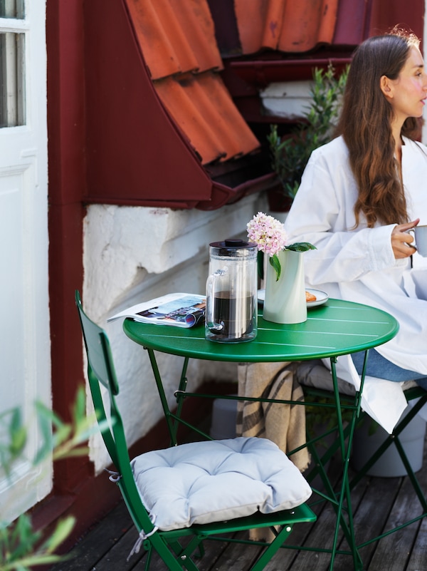 SUNDSÖ green metal chair and table set on a balcony, a woman drinks coffee 