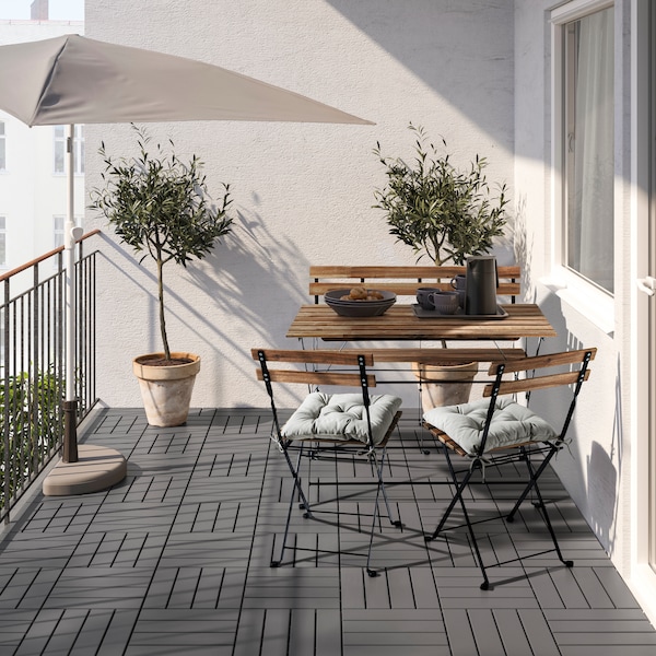 A balcony withTARNO table and chairs decorated with grey RUNNEN decking, a parasol, and plants