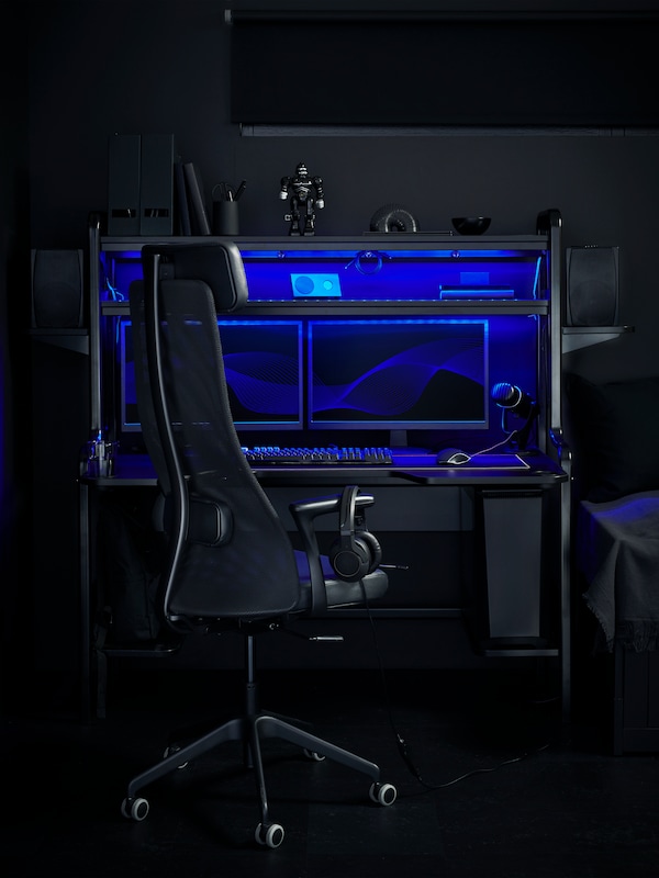 An IKEA FREDDE black gaming desk lit with blue neon lights, and a matching black gaming chair.