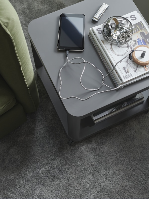 An IKEA TINGBY side table in dark grey over a dark grey rug, various magazines and a phone over it.