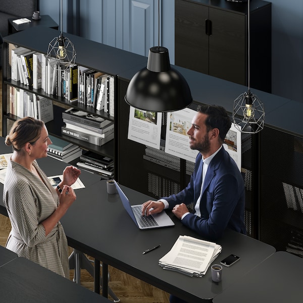 An office setting where a woman talks to a man in a suit who sits with his laptop by a TOMMARYD table.
