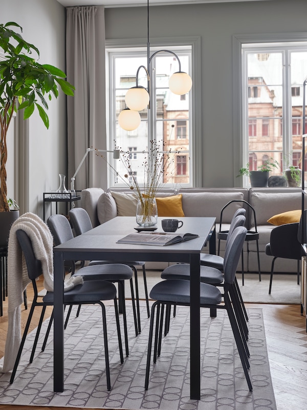 An IKEAVANGSTA dining table in black brown with grey dining chairs, in a bright dining room with white floors and a grey rug.