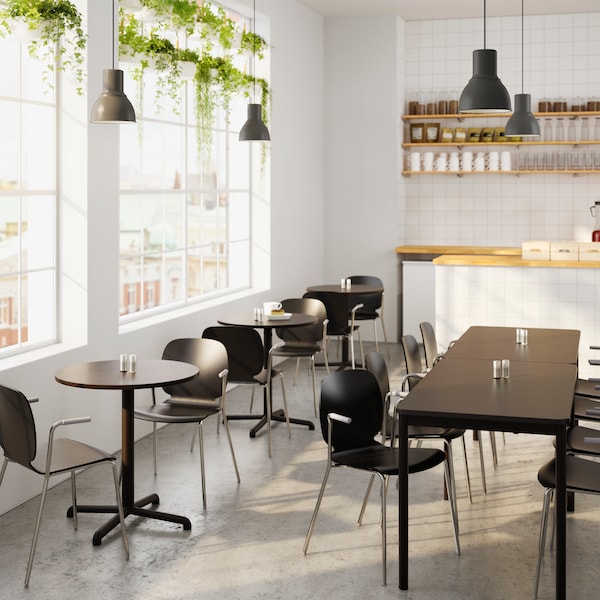 A bright café with white tables, black chairs, a counter area with a coffee machine and a black and white menu board.