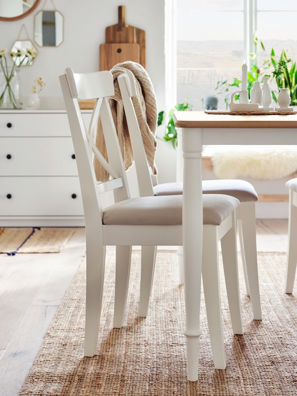 Two IKEA INGOLF dining chairs in a traditional style, in a white colour with beige upholstered seat, on top of a jute rug.