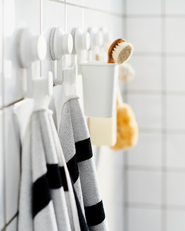 Five white TISKEN hooks with suction cups hanging in a row on a bathroom wall, holding striped towels, sponges and brushes.