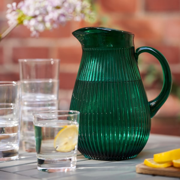An IKEA SÄLLSKAPLIG jug in patterned green on a table with glasses.